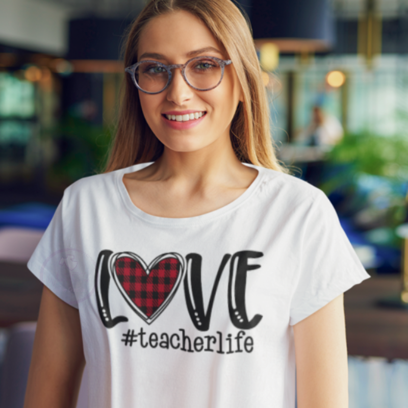 White tee with Love teacher life; love is spelled with a heart (buffalo plaid) for the O